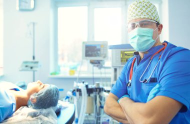 Ameliyat odasında arka planda erkek cerrah var..