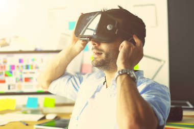 Genç erkek yazılım programcısı ofiste üç boyutlu sanal gerçeklik gözlükleriyle yeni bir uygulama test ediyor.