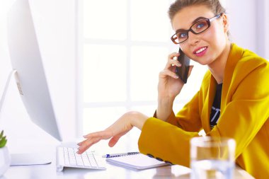 İş kadını ofiste bilgisayar ve cep telefonu kullanarak işine konsantre oluyor..