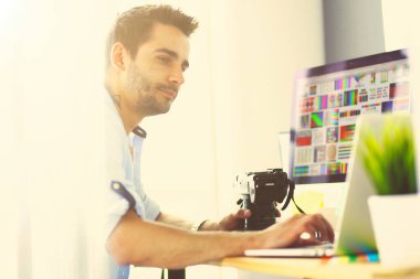 İnternette çalışırken bilgisayarın ve dizüstü bilgisayarın önünde grafik stüdyosunda oturan genç tasarımcının portresi
