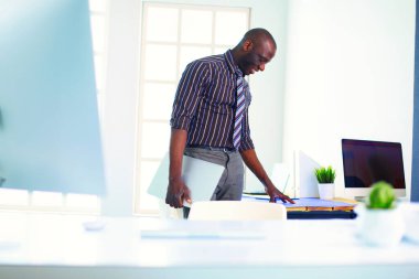 Ofiste bilgisayar ve planlarla çalışan Afrikalı Amerikalı bir mimar..