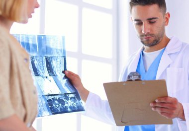 Yakışıklı doktor genç bayan hastasıyla konuşuyor ve ofisinde otururken notlar alıyor.