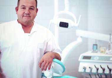 Diş kliniğinde duran gülümseyen bir dişçinin portresi..