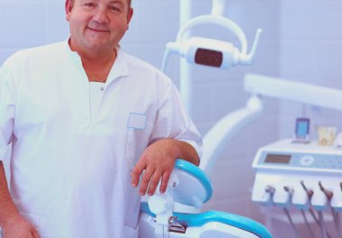 Diş kliniğinde duran gülümseyen bir dişçinin portresi..
