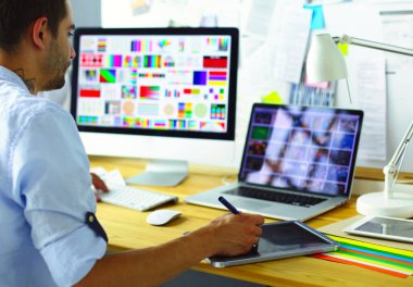 İnternette çalışırken bilgisayarın ve dizüstü bilgisayarın önünde grafik stüdyosunda oturan genç tasarımcının portresi