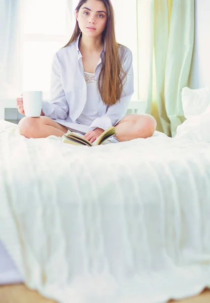 Γυναίκα Που Κάθεται Στο Κρεβάτι Διαβάζοντας Ένα Βιβλίο Και Τρώγοντας — Φωτογραφία Αρχείου