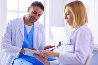 Yakışıklı doktor genç bayan doktorla konuşuyor ve ofisinde otururken notlar alıyor.