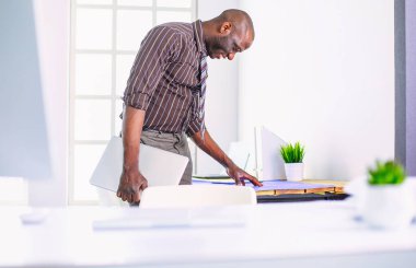 Ofiste bilgisayar ve planlarla çalışan Afrikalı Amerikalı bir mimar..