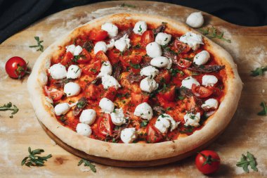Çeri domatesli bir Margherita pizzası, mozzarella dilimleri ve fesleğen ahşap bir kabuğun üzerinde duruyor..