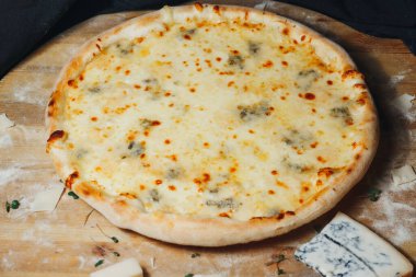 Erimiş peynirle kaplanmış yeni pişmiş bir pizza, ahşap bir tahta kesme tahtasının üzerinde oturur..