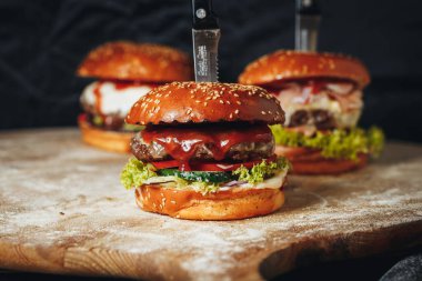 Tahta bir kesme tahtasının üzerinde dilimlenmeye hazır keskin bir bıçakla güzelce sergilenen üç sulu hamburger..