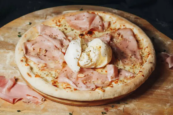 stock image A freshly baked pizza topped with savory ham and gooey cheese sits on a rustic wooden cutting board.