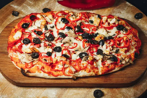 Zeytin ve biberli yeni pişmiş bir pizza. Köy ahşap kesim tahtasının üzerinde dinleniyor..