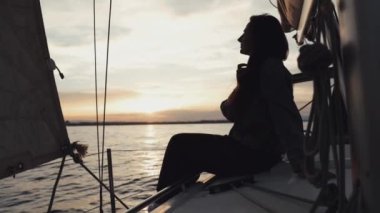 Bir kadının, gün batımının sıcak renkleriyle çevrili bir yelkenlide otururken huzur içinde düşünmesine tanık olun..