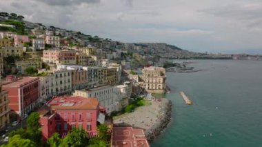 Ünlü bir seyahat noktasında deniz kıyısında ilerliyorlar. Suyun üstündeki yamaçtaki saraylar ya da otel binaları. Napoli, İtalya.