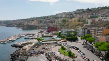 Seyahat yerindeki turizm merkezinin üzerinden uçuyor. Deniz kıyısındaki lüks tarihi saraylar ve restoranlar. Yat ve yelkenliler limana demirlemiş. Napoli, İtalya.