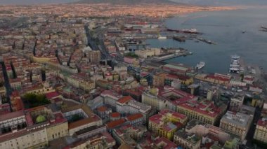 Şehir merkezindeki şehir ve limandaki şehir gelişiminin yüksek açılı görüntüsü. Eğim, batan güneş tarafından aydınlatılan Vezüv yanardağını ortaya çıkarıyor. Napoli, İtalya.