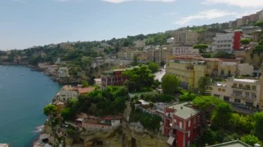 Güneşli bir günde deniz kıyısındaki kayalıklardaki dik yamaçlardaki lüks tarihi binaların sinematik görüntüleri. Napoli, İtalya.