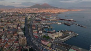 Liman ve sahil boyunca uzanan ana yol üzerinde ilerliyorlar. Vezüv Dağı, güneşi uzak tutarak aydınlandı. Napoli, İtalya.
