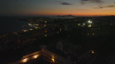 Gece geç saatlerde şehrin üstündeki tepedeki manastır ve şatonun üzerinden ileriye doğru uçuyor. Napoli Körfezi 'nin panoramik görüntülerine karşı romantik alacakaranlık gökyüzü. Napoli, İtalya.