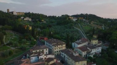İleri binaların ve bahçelerin üzerinden uçar ya da şehrin yukarısındaki yamaçlara park eder. Alacakaranlıkta şehrin kenar mahallelerinin havadan görüntüsü. Floransa, İtalya.