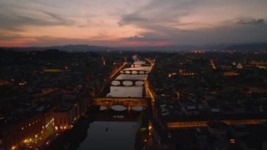 Romantik şehir manzarası. İleriye doğru Arno nehri üzerinde uçar alacakaranlıkta renkli gökyüzünü yansıtır. Rıhtımlar ve köprüler aydınlatıldı. Floransa, İtalya.