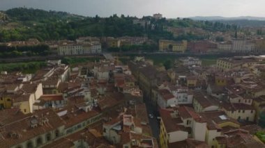 Şehir merkezindeki binaların üzerinde ilerliyorlar. Arno nehri üzerinde yol köprüsü açılıyor. Su yüzeyi karşı kıyıdaki evleri yansıtıyor. Floransa, İtalya.