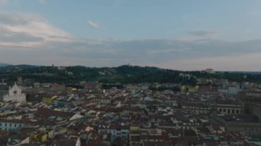 Alacakaranlıkta tarihi şehir merkezindeki eski binaların üzerinden ileriye doğru uçar. Park ya da arka planda ağaçların yükseldiği bahçeler. Floransa, İtalya.