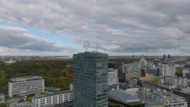 Üzerinde büyük Mercedes Benz logosu olan modern yüksek katlı ofis binasının etrafında dolaş. Arka planda sonbahar yeşillikleri olan bir park. Charlottenburg Mahallesi, Berlin, Almanya.