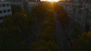 Şehir merkezindeki geniş cadde boyunca ağaçların üzerinden uçuyor. Eğim, batan güneş ve inşaat alanının siluetini ortaya çıkarıyor. Charlottenburg Mahallesi, Berlin, Almanya.