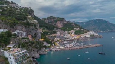 Gün batımında çekici turistlerin inanılmaz yüksek hızlı görüntüleri. Deniz kıyısının yukarısındaki dik yamaçlarda binalar ve yollar. Amalfi, İtalya.