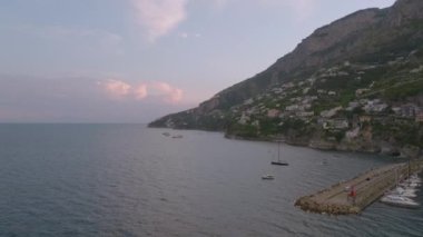 Deniz kıyısında demirlemiş teknelerin romantik manzarası. Sudan yükselen dik yamaçlar, denizin üstündeki kayalıklardaki apartmanlar. Amalfi, İtalya.