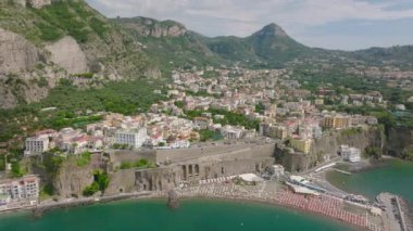 Şehrin ve deniz kenarındaki tepelerin hava kaydırak ve pan görüntüleri. Sahilde güneş gözlüğü sıraları. Amalfi, İtalya.