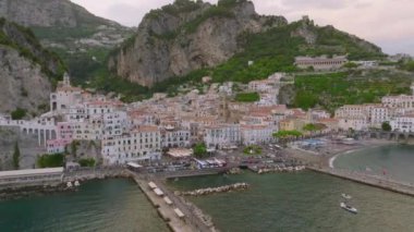 Deniz kıyısındaki tarihi kasabanın hava kaydırağı ve pan görüntüsü. Gezinti güvertesi, sahil ve yüksek kayalar arasındaki binalar. Amalfi, İtalya.