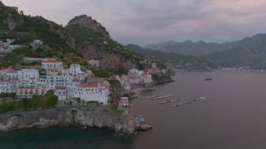 Akdeniz 'deki binaların etrafında alacakaranlıkta uçun. Deniz kıyısındaki yamaçlarda binalar ve yollar. Amalfi, İtalya.