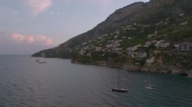 Yolculuk varış noktasında deniz kıyısında suyun üzerinde uçar. Denizin yukarısındaki yamaçta inşa edilmiş binalar. Amalfi, İtalya.
