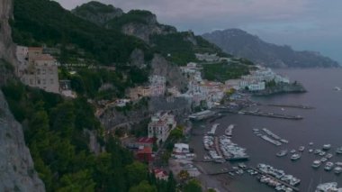 Marinalı deniz koyunun havadan panoramik manzarası ve alacakaranlıkta kayalık uçurumlar arasında tarihi bir kasaba. Amalfi, İtalya.