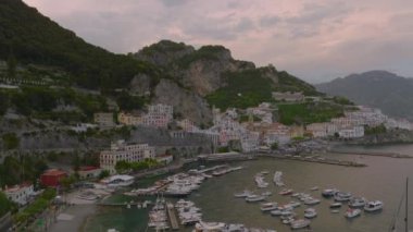 Arka plandaki tarihi kentteki limanlara ve eski binalara parkedilmiş teknelerin yüksek kaydırak ve pan görüntüsü. Amalfi, İtalya.