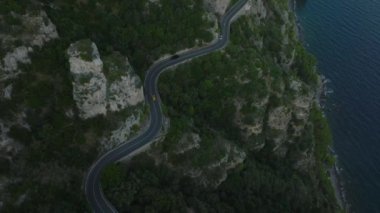 Yüksek açılı, deniz kıyısındaki kayalıklarda dönen panoramik yolda ilerleyen arabaların görüntüsü. Güzel manzarayı gözler önüne seriyor. Amalfi, İtalya.