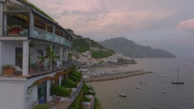 Suyun üzerindeki lüks daireler boyunca sıkı bir uçuş. Yat limanındaki tekneleri ve tarihi kasabanın etrafındaki tepelik kıyı manzarasını gözler önüne seriyor. Amalfi, İtalya.