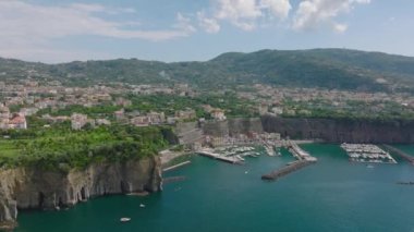 Yat ve yelkenliler limana demirlemiş. Deniz kıyısında geriye doğru uç. Turkuaz su yüksek kaya kayalıklarıyla kaplı. Amalfi, İtalya.