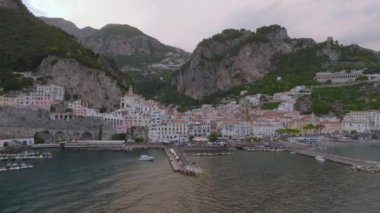 Yüksek kayalıklar arasında bulunan deniz kıyısındaki ünlü kasabanın panoramik manzarası. Alacakaranlıkta rıhtım ve tarihi binalar. Amalfi, İtalya.