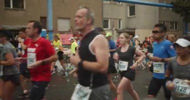 Şehirdeki spor müsabakalarında yiyecek içecek alanından geçen bir grup koşucu. Maraton koşu yarışı, Berlin, Almanya.