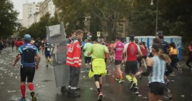 Sağlık görevlileri şehir caddesinde koşan atletlerin arasında yürüyor. Maraton koşu yarışı, Berlin, Almanya.