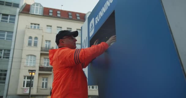 身穿鲜活橙色风衣的男子在横幅上安装时间显示屏 城市街道上的体育之夜 马拉松比赛 德国柏林 — 图库视频影像