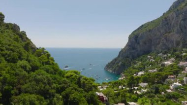 İleri doğru yemyeşil bitki örtüsünün üzerinde uçar. Deniz kıyısındaki çekici turistlerin panoramik manzarasını gözler önüne seriyor. Capri, Campania, İtalya.