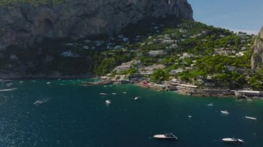 Ön taraflar turkuaz suyun üzerinde uçar. Plaja doğru gidiyor ve turistik tatil beldesindeki deniz kıyısındaki restoranlara gidiyor. Capri, Campania, İtalya.