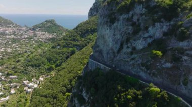 İleri doğru yüksek kaya duvarları boyunca uçar. Araçlar uçurumun etrafındaki dar virajlı yolda gidiyor. Capri, Campania, İtalya.