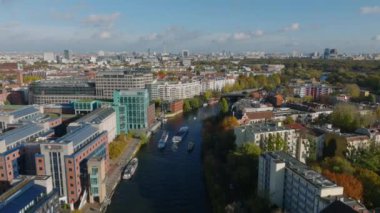 Spree nehrinin üzerinden uçup şehrin içinden geçiyor. Tekneler rıhtımlarda binaların etrafından geçiyor. Şehir, şehir egemenliği altında. Berlin, Almanya.