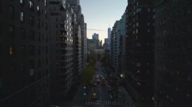 Uzun apartmanlarla çevrili caddedeki trafiğin hava görüntüsü. Gün batımında şehrin üzerinde uç. New York City, ABD.